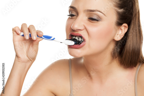 young woman brushing her teeth with black toothpaste of activated charcoal on white background
