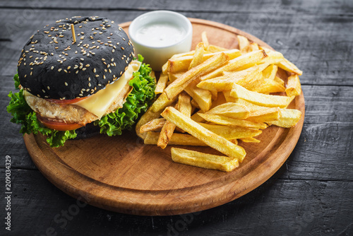 Tasty burger from black bun with frenck fries on wooden board