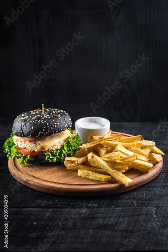 Tasty burger from black bun with frenck fries on wooden board