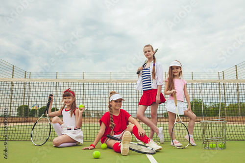 Portrait of group of girls as tennis players holding tennis racket against green grass of outdoor court © master1305