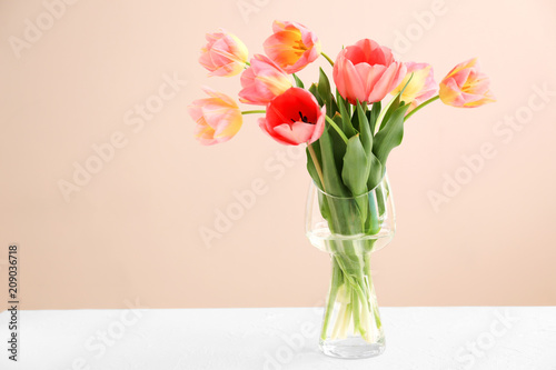 Vase with beautiful tulips on table against color background