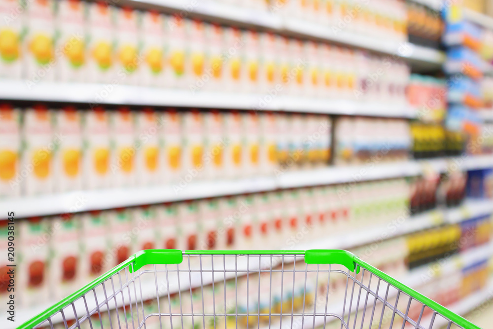 Supermarket with fruit juice product shelves interior blur background with empty shopping cart