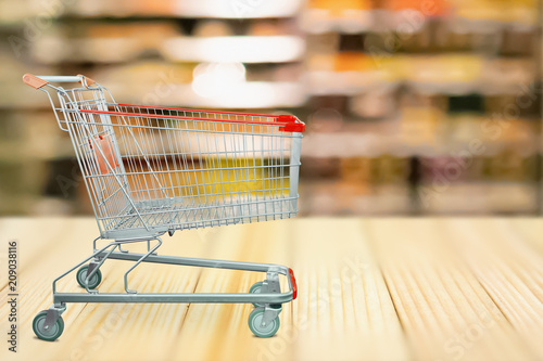 Abstract blur supermarket shelves defocused background with shopping cart on wood table