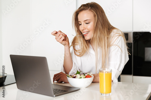 Cheerful young woman eating salad from a bowl