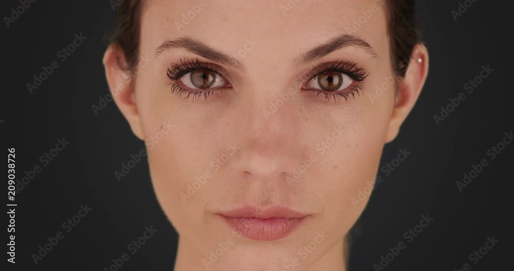 Portrait of pretty brunette gazing at camera seriously on solid dark gray backdrop, Frontal view of attractive woman looking at the camera on dark background, 4k