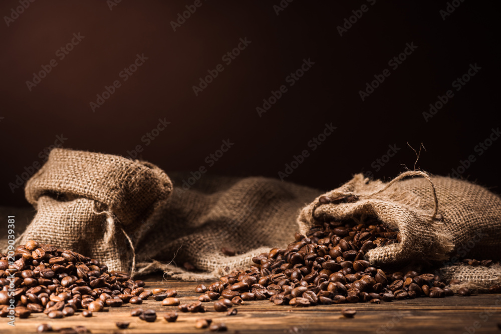 sacks of coffee beans on rustic wooden table on dark brown background sacks of coffee beans on rustic wooden table on dark brown background