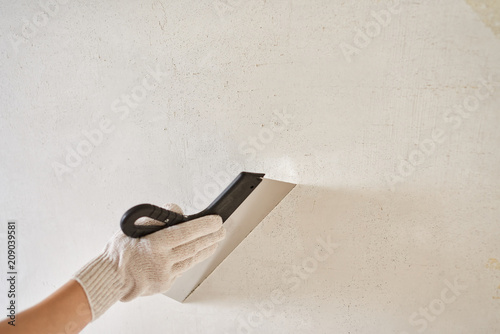 Spatula with putty in hand. Worker puts of plaster on wall.