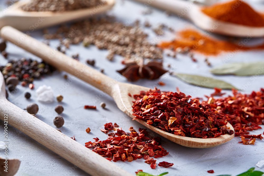 Red hot chillies pepper flakes in wooden spoon on white textured background, top view, close-up, selective focus. Red hot chillies pepper flakes in wooden spoon on white textured background, top view, close-up, selective focus.
