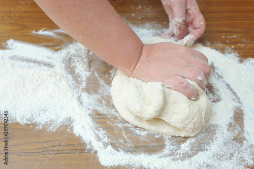 Women's hands knead the dough in the kitchen on the table. Close-up