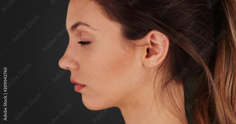 Closeup profile of beautiful white female standing alone on dark gray background, Profile portrait of pretty millennial female looking off into distance on grey background, 4k