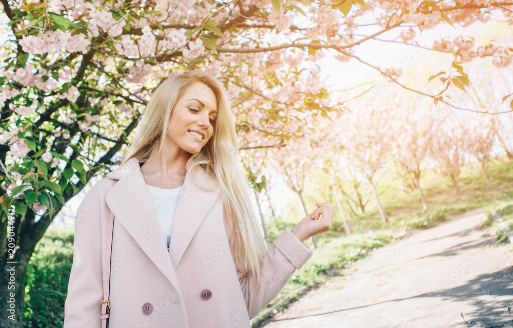 Young beautiful woman in a pink coat posing with flowers in garden. Park. Young beautiful woman in a pink coat posing with flowers in garden. Park.