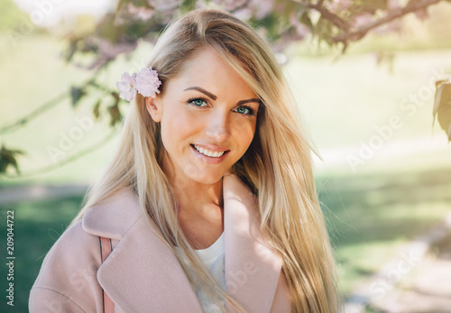 Young beautiful woman in a pink coat posing with flowers in  garden. Park.