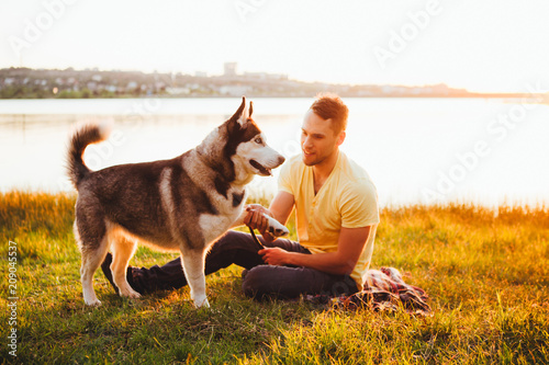 A young man is sitting on the grass with a hussy breed dog.