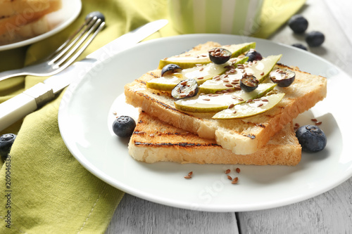 Tasty sweet toasts with sliced pear and blueberry on plate