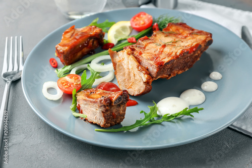 Plate with delicious grilled ribs, sauce and vegetables on table