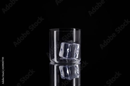 glass with ice cube on reflective surface isolated on black