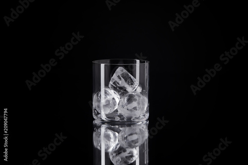 single glass with ice cubes on reflective surface isolated on black