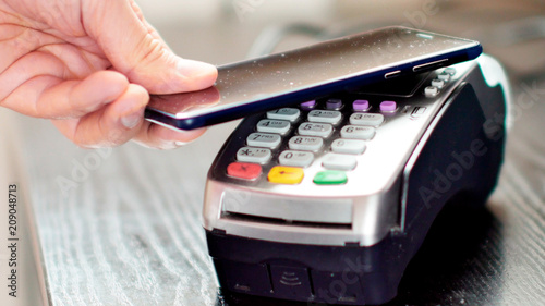 Customer paying with NFC technology by mobile phone on POS terminal.