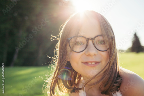 Girl looking at camera in nature against sunset. Summer leisure. Girl in glasses with black rim.