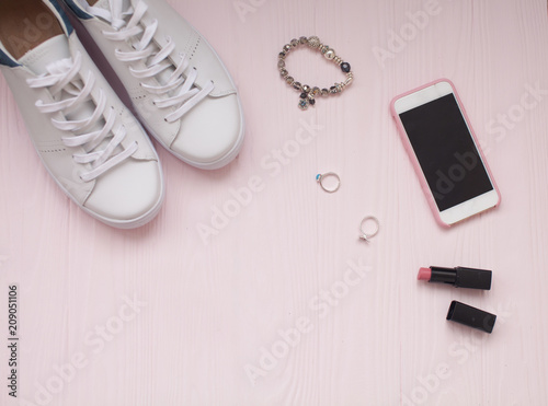 women's accessories - bag, sneakers, earrings, rings, lipstick on wooden pink background, top view
