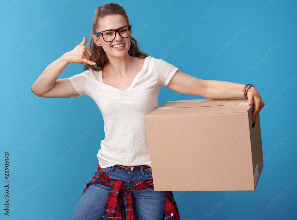 woman with cardboard box showing call me gesture on blue