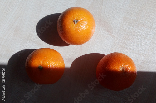 Three oranges lie on a wooden table in the form of a triangle illuminated by a bright morning sun with sharp shadows