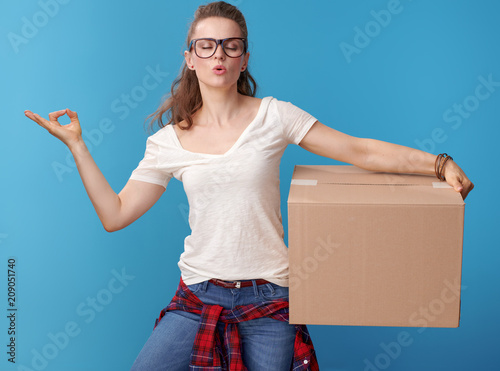 relaxed active woman with cardboard box doing yoga on blue
