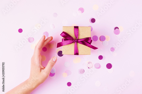 Woman hand and kraft gift box with pink bow on pink background decorated with...