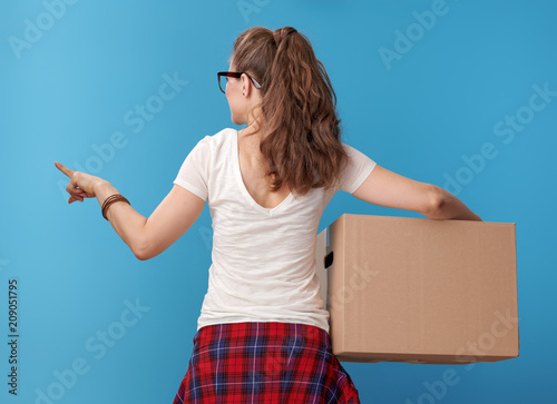 modern woman with cardboard box pointing at something on blue