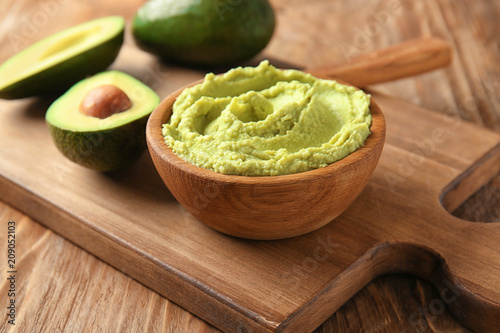 Bowl with tasty guacamole and ripe avocado on wooden board photo