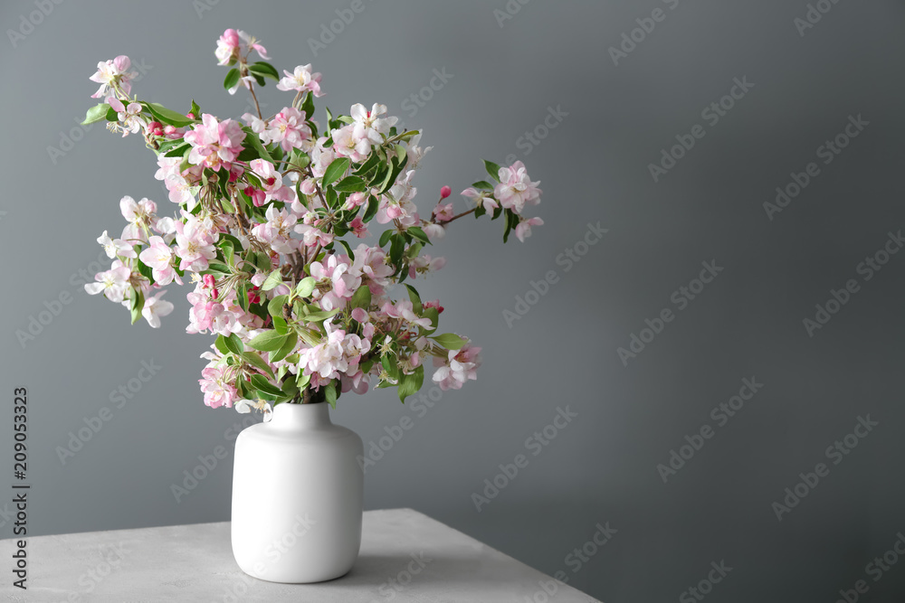 Vase with beautiful blossoming branches on table against grey background Vase with beautiful blossoming branches on table against grey background