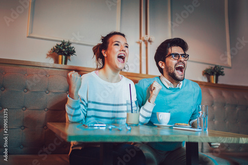 Modern couple in cafe looking excited and happy after their favorite football team scored a touchdown.