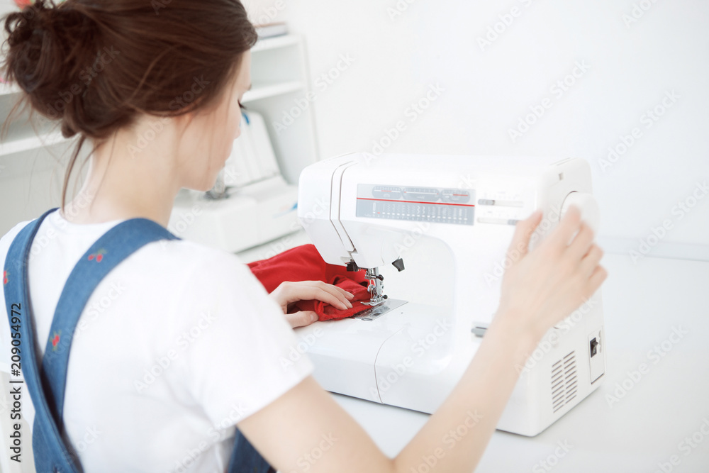 Happy attractive young woman seamstress sitting and sews on sewing machine in studio
