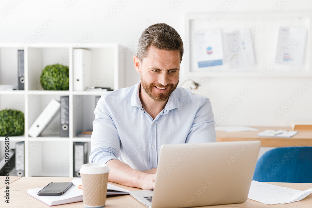Happy bearded man sitting in office working Happy bearded man sitting in office working