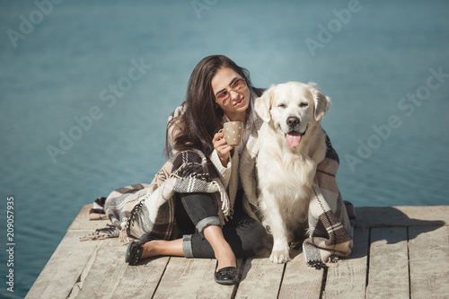 Young attractive woman sitting at the pier with her dog. Best friends outdoors