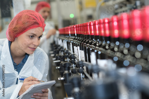 Woman making notes beside bottling plant production line photo