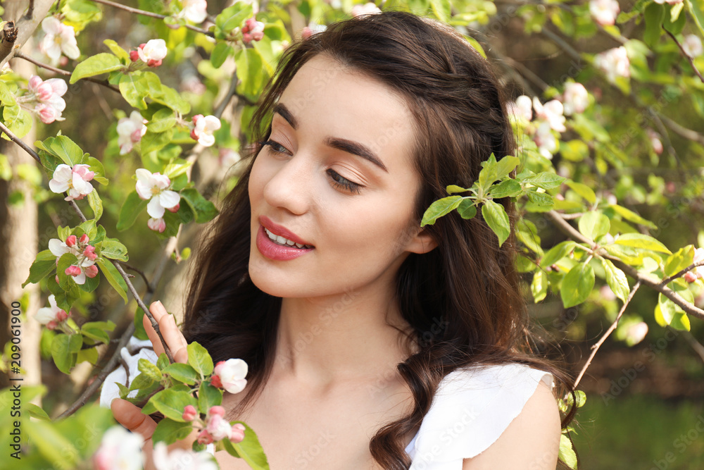 Fototapeta premium Beautiful young woman near blossoming tree on sunny spring day