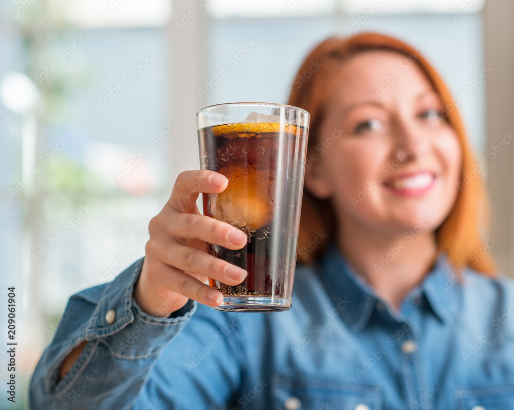 Redhead woman holding soda refreshment with a happy face standing and smiling with a confident smile showing teeth Redhead woman holding soda refreshment with a happy face standing and smiling with a confident smile showing teeth