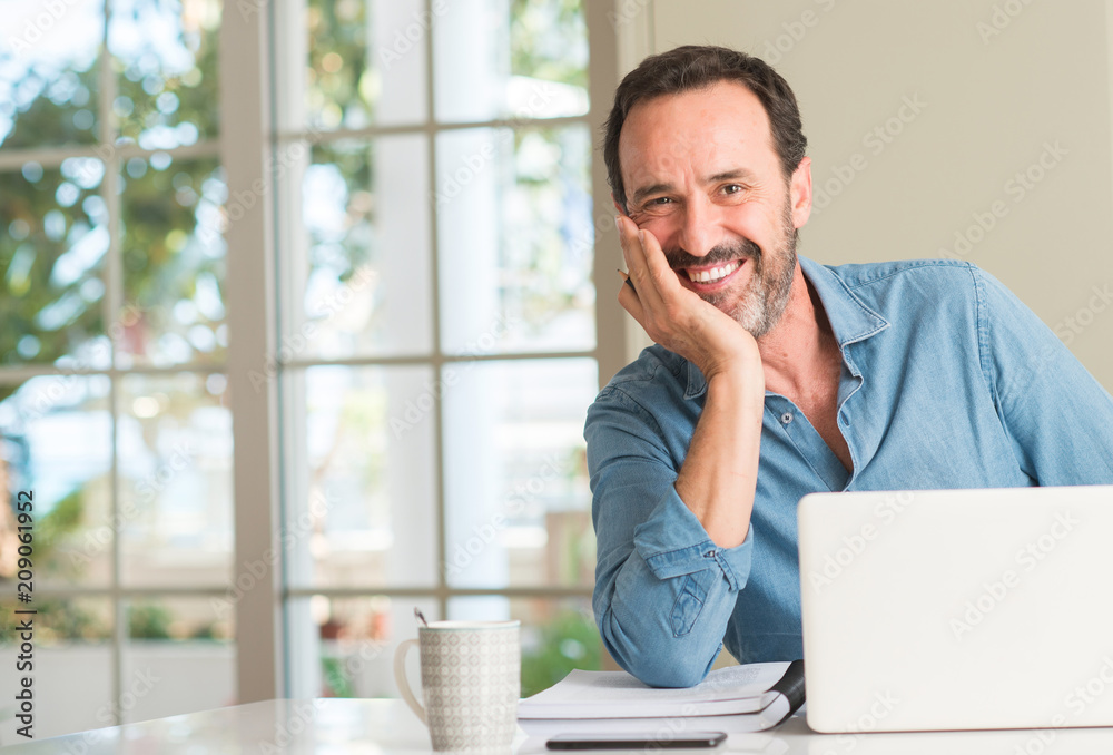 Middle age man using laptop at home with a happy face standing and smiling with a confident smile showing teeth Middle age man using laptop at home with a happy face standing and smiling with a confident smile showing teeth