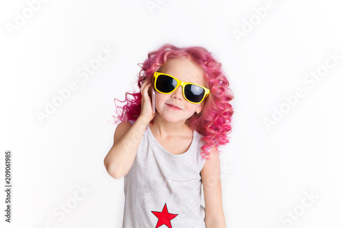 Colored wavy hairs. Little modern hipster girl in fashion clothes in sunglasses talking by the phone. Studio
