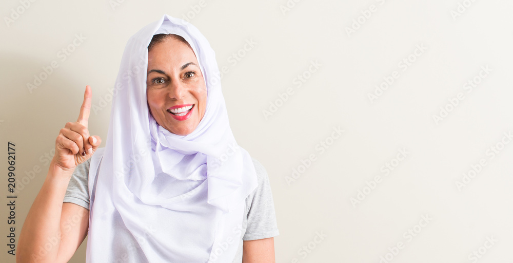 Middle age arabian woman wearing white hijab surprised with an idea or question pointing finger with happy face, number one Middle age arabian woman wearing white hijab surprised with an idea or question pointing finger with happy face, number one