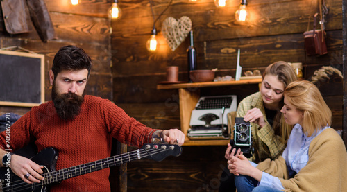 Macho with brutal face holding electric guitar. Bearded man playing musical instrument. Man with hipster beard rehearsing new song, music concept. Woman and teen girl recording musical performance