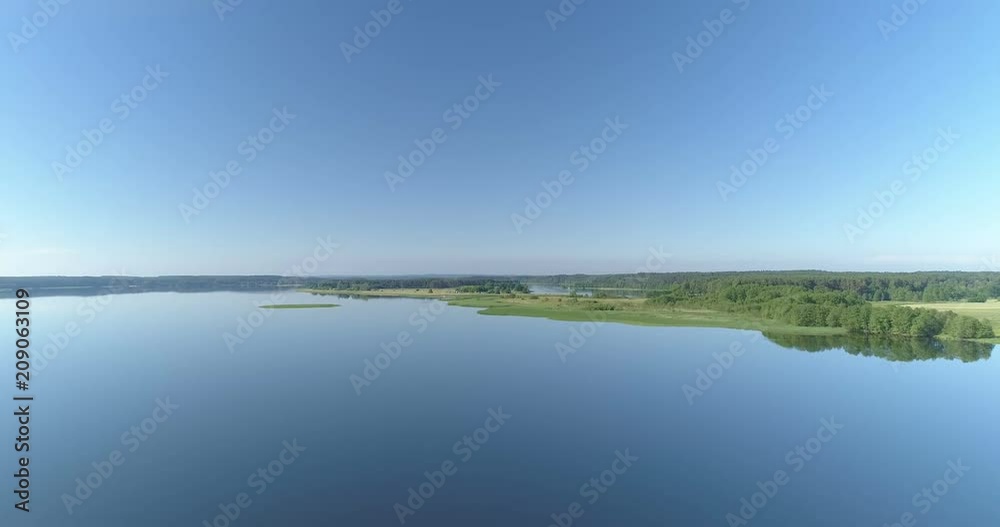 Fast flight over idyllic lake with glass calm surface green forest and blue sky Fast flight over idyllic lake with glass calm surface green forest and blue sky