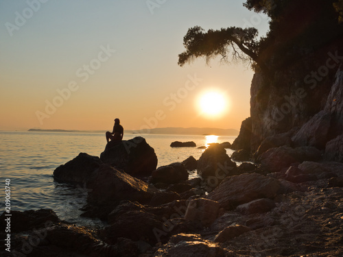 Sihouette of a girl sitting on a rock at sunset, Kastani Mamma Mia beach, island of Skopelos, Greece