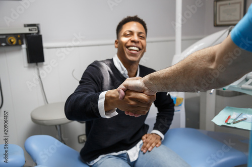 Young African-American man shaking hand of crop dentist having visit in medical clinic. 