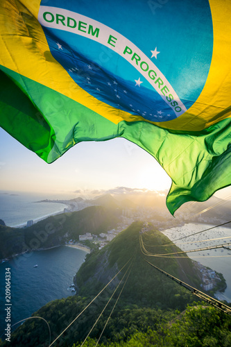 Brazilian flag shines above the golden sunset city skyline at Sugarloaf Mountain in Rio de Janeiro Brazil. 