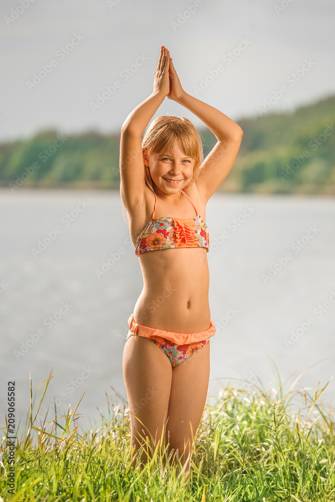 little girl with light hair standing in a swimsuit in the summer against a  river Stock Photo