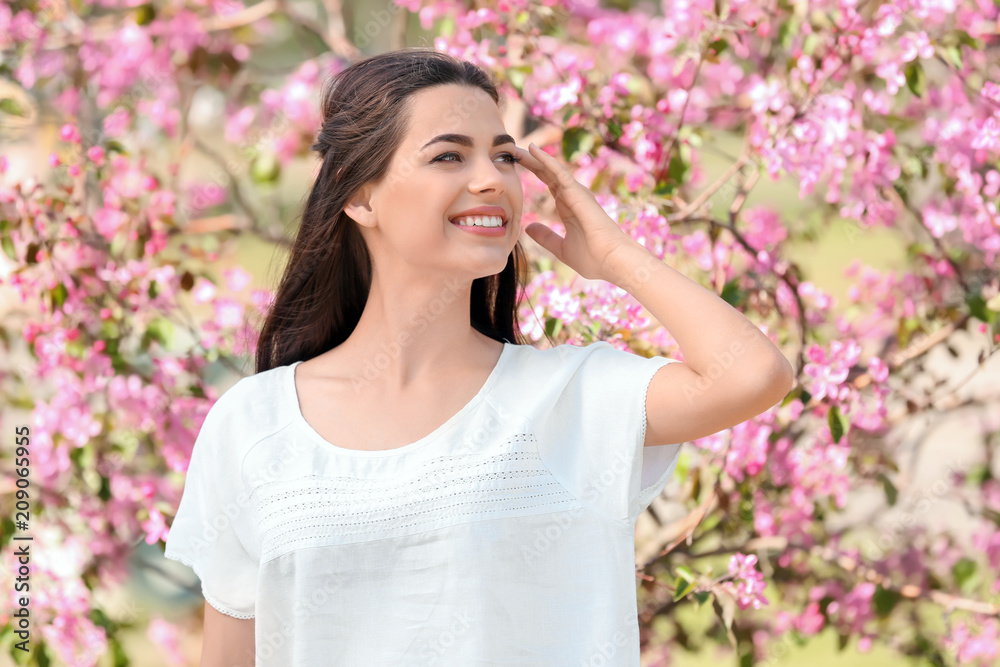Beautiful young woman near blooming tree in park on spring day Beautiful young woman near blooming tree in park on spring day