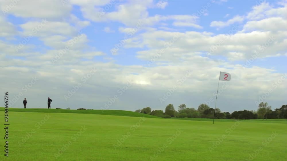 Green golf course with white flag and the hole. Sport, relax, recreation and leisure concept. Summer landscape on a bright sunny day with cloudy sky Green golf course with white flag and the hole. Sport, relax, recreation and leisure concept. Summer landscape on a bright sunny day with cloudy sky