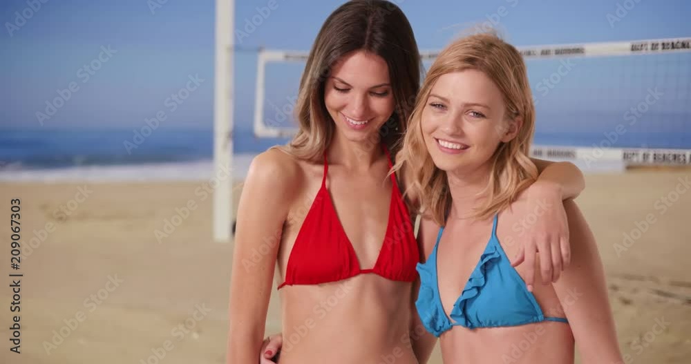 Gorgeous blonde and brunette in bikinis posing with joy at the beach by volleyball net, Two fit girls smiling at the camera while at the beach on a nice day, 4k Gorgeous blonde and brunette in bikinis posing with joy at the beach by volleyball net, Two fit girls smiling at the camera while at the beach on a nice day, 4k
